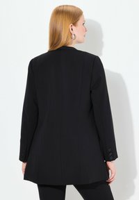 Blazer nero con una vestibilità sartoriale, maniche lunghe e dettagli a tre bottoni sui polsini. Tessuto liscio con un design strutturato.