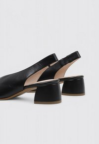 Zapatos de cuero negro tipo slingback con punta redonda y tacón grueso y texturizado. Presentan una superficie suave y un diseño minimalista.