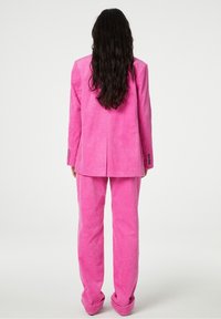 Completo di velluto a coste rosa con giacca su misura e pantaloni abbinati. Presenta un taglio dritto e un tessuto testurizzato. Dettagli posteriori visibili della giacca.