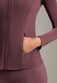 Lila atletisk jacka med full dragkedja, smal passform, långa ärmar och sidofickor, gjord av ett mjukt, stretchigt tyg.