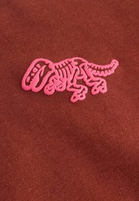 Eine Nahaufnahme eines dunkelbraunen Stoffes mit einem pinken skelettartigen Dinosaurier-Design, das seinen abstrakten, verspielten Stil zeigt.