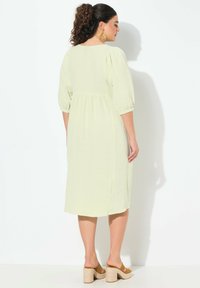 Ljust grönt texturerat klänning med trekvarts puffärmar och ett lager på lager nederkant. Kombinerad med beige blockklacksandaler.