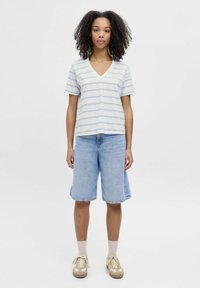 Camiseta de rayas en azul claro y blanco con escote en V, combinada con pantalones cortos de denim hasta la rodilla. Los accesorios incluyen calcetines de color claro y zapatillas beiges.