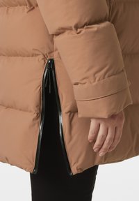 Giacca a vento marrone con una texture liscia e lucida e dettagli con cerniera laterale. La manica presenta un ampio polsino e un design trapuntato e imbottito.
