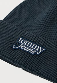 Căciulă tricotată cu model în dungi de culoare albastru închis, având un logo brodat „tommy jeans” alb pe o etichetă albastru închis. Textură moale, potrivire comodă.