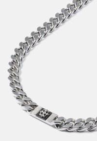 Chunky silver curb chain necklace with polished interlocking links and a rectangular clasp featuring a decorative floral emblem.