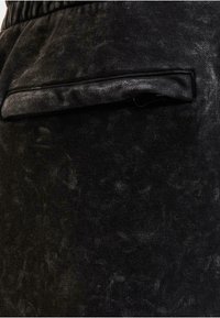 Svart texturerad tyg med en lätt lyster, som har en plan bakficka med en slät svart kant. Tyget verkar mjukt och något fläckigt.