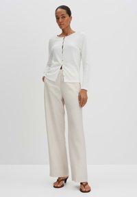 White button-up cardigan with long sleeves, textured fabric, and round neckline, paired with beige wide-leg pants and brown sandals.