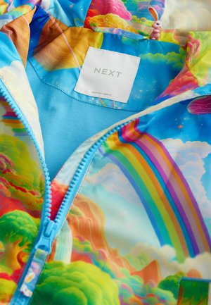 Färgglad, mönstrad zip-up jacka med en blå bas och regnbågs- samt landskapsdesign. Lappen inuti visar "NEXT", tillverkad i Myanmar.
