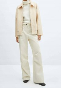 Světlý béžový cropped fleecový kabát, krémový rolák a široké béžové kalhoty. Hladká textura, minimalistický design a dva detaily kapes.