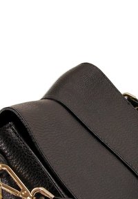 Zwarte leren handtas met een gestructureerde afwerking, uitgerust met een brede schouderband en gouden hardwareaccenten. Het ontwerp benadrukt zachte rondingen en hoeken.