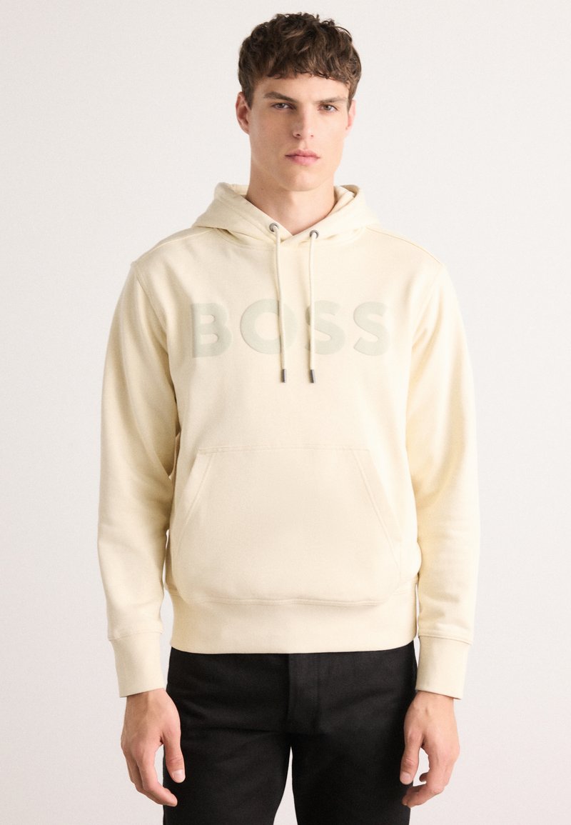 Sudadera crema con un bolsillo frontal, capucha con cordón y un gran logo "BOSS" desvanecido en el pecho; tejido suave y corte relajado.