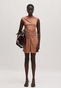 Bruin aansluitend topje met een geraffineerd ontwerp, gecombineerd met losse shorts en een grote donkerbordeaux handtas. Sandalen maken de look compleet.