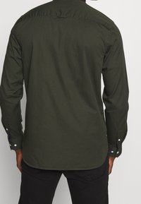 Langarmshirt in donkergroen, gemaakt van katoen. Beschikt over knoopmanchetten, een afgeronde zoom en een rugpasdetail. Glad van structuur.