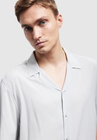 Jasnoszara koszula z krótkim rękawem, gładki materiał, otwarty kołnierz, zapięcie na guziki, luźny krój, minimalistyczny design, bez wzorów ani akcentów.