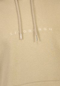 Sudadera beige con un tejido texturizado, cordones con puntas plateadas y el nombre de la marca "LINDBERGH" bordado en blanco.