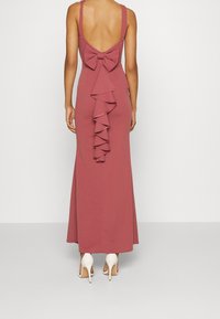 Langes, figurnahes Kleid in staubigem Pink mit breiten Trägern, einem tiefen V-Ausschnitt am Rücken und einer großen Schleifendetail an der Taille, das eine Rüschelement aufweist.