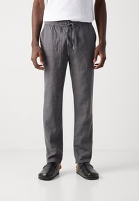 Gray linen pants with an elastic waistband and drawstring. Features side pockets and a relaxed fit. Worn with black clogs and a white shirt.