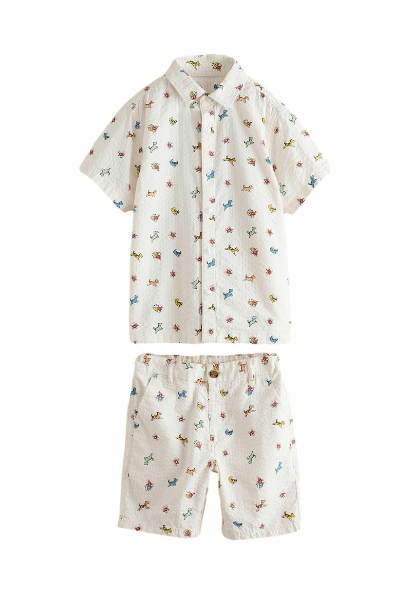 Set di camicia a maniche corte e pantaloni corti in tessuto bianco con motivi colorati di cani e fiori. Chiusura con bottone sui pantaloni corti. Materiale testurizzato.