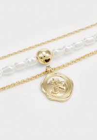Collar de tres capas con cadena de oro, perlas y un colgante dorado con diseños en relieve de ancla y corazón.