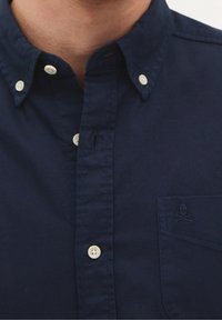 Marineblaue Hemdjacke aus Baumwollstoff. Mit einem Button-Down-Kragen, weißen Knöpfen und einem kleinen Totenkopf-Logo auf der Brusttasche.