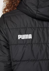 Musternud musta puhvers jope horisontaalsete õmblustega, millel on valge "PUMA" logo vasakul ülaservas. Pehme sünteetiline materjal.