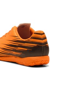 Oranges Fußballschuh mit einer strukturierten Oberseite, die schwarze Farbverläufe aufweist, und einer strukturierten Gummisohle. Die Ferse hat eine minimale Polsterung.