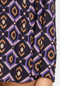 Multicolored blouse featuring a geometric pattern with purple, brown, and beige shapes on a black background. Soft, flowing fabric.
