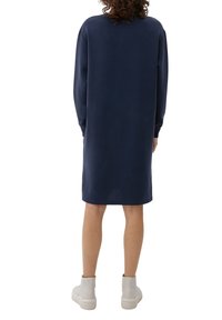 Navyblå sweatshirtklänning med långa ärmar, rak sk ärning, sidoflikar och en mjuk textur, kombinerad med vita ankelstövlar.