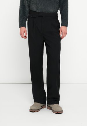 Svarte bukser med skreddersydd passform, legg og en knappedetalj. Laget av glatt stoff; kombinert med lysegrå ankelstøvletter.