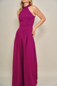 Fukszia overál pántos nyakkal, testhez simuló felsőrésszel és széles, redőzött szárakkal. Simább, rugalmas anyagból készült, matt felülettel.