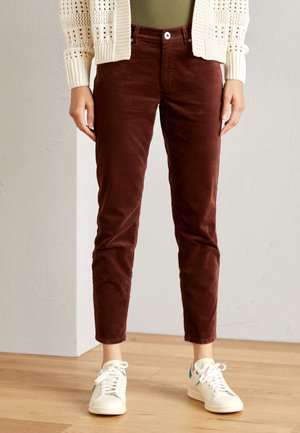 Elastyczne ciemnobrązowe sztruksowe spodnie wąskiego kroju noszone z białymi trampkami i kremowym, dzianym kardiganem na oliwkowozielonej bluzce.