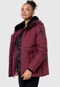 Maroon puffer jacket with a faux fur collar, zippered pockets, quilted design, and a branded patch on the left sleeve. Soft material.