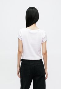 Short-sleeve, light pink cotton T-shirt with a round neckline, paired with high-waisted black denim jeans featuring back pockets.