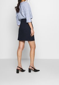 Blårandig långärmad skjorta med uppvikt ärm, som matchas med en mörk marinblå kjol och svarta klackskor med slingback och textur.