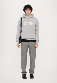 Grauer Kapuzenpullover mit floralem Design, kombiniert mit karierter Hose. Schwarze Umhängetasche, schwarze Schuhe und ein geschichteter schwarzer Sweatshirt sichtbar.