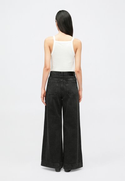 Laiad seelikuga mustad teksapüksid, valmistatud denimist, kõrge vöökohaga ja tagataskutega, kombineeritud vormitud valge topiga. Minimalistlik disain, sile tekstuur.