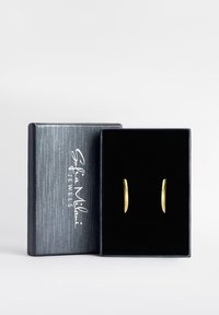 Orecchini a cerchio dorati esposti in una scatola grigia testurizzata foderata in velluto nero. La scatola presenta testo argentato e un design semplice.