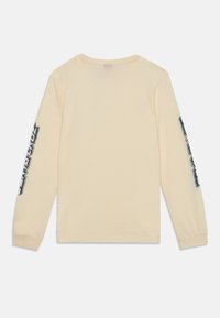 Långärmad skjorta i mjuk beige bomull, med svarta textgrafiker på båda ärmarna. Rundad halsringning och avslappnad passform.
