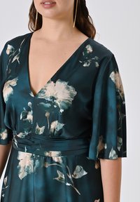 Blaugrün gemustertes Kleid mit floralem Muster, tiefem V-Ausschnitt, flatternden Ärmeln und tailliertem Bündchen, aus glattem Stoff gefertigt.