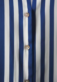 Button-up shirt featuring vertical blue and white stripes, with round, shiny buttons down the front and smooth fabric texture.
