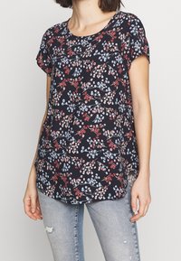Blusa de manga corta de color azul marino con patrón floral en rojo y azul, escote redondo y aberturas laterales, hecha de tejido ligero.