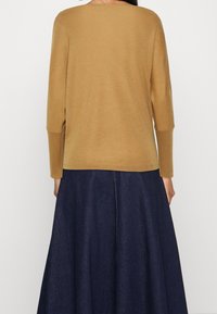 Långärmad, senapsgul topp i mjukt material med rund halsringning och avslappnad passform, kombinerad med en mörk denimkjol.