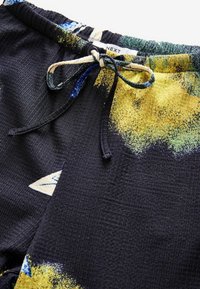 Shorts noirs à motifs avec un tissu texturé, présentant des designs abstraits jaunes et verts et une taille à cordons.