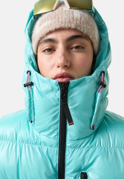 Eine türkisfarbene Daunenjacke mit hohem Kragen, Reißverschluss und kontrastierendem schwarzen Reißverschluss. Sie verfügt über Kordelzug-Akzente und eine glänzende Textur.