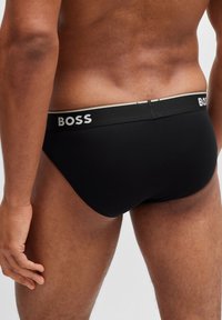 Black brief underwear with a branded elastic waistband featuring BOSS in white. Smooth texture, snug fit, and mid-rise design.
