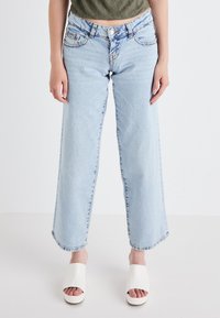 Heled sinised laiad säärised teksad, mis on valmistatud denimist, kõrge vöökohaga ja klassikalise viie taskuga disainiga, paired valgete platvormsandaalidega.