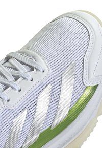 Weiße Mesh-Sportschuhe mit silbernen Streifenakzenten und einem grünen Seitendetail. Sie verfügen über runde Schnürsenkel und eine strukturierte Gummisohle.