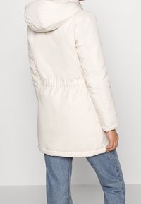 Lightweight white puffer jacket with a hood, cinched waist, and long sleeves. Features a smooth, shiny texture and elastic cuffs.