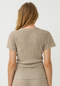 Lichtbruine gestreepte top met korte mouwen en een ronde halslijn. De textuur heeft verticale ribbels. Eenvoudig, minimalistisch ontwerp.